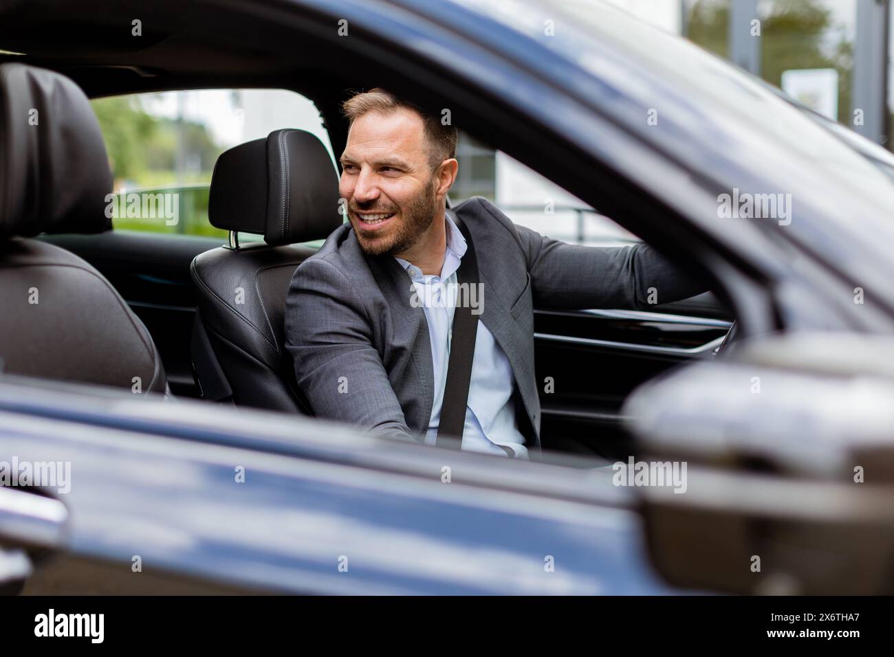 Il conducente sorride mentre tiene il volante, guidando lungo la strada in un veicolo ben equipaggiato Foto Stock