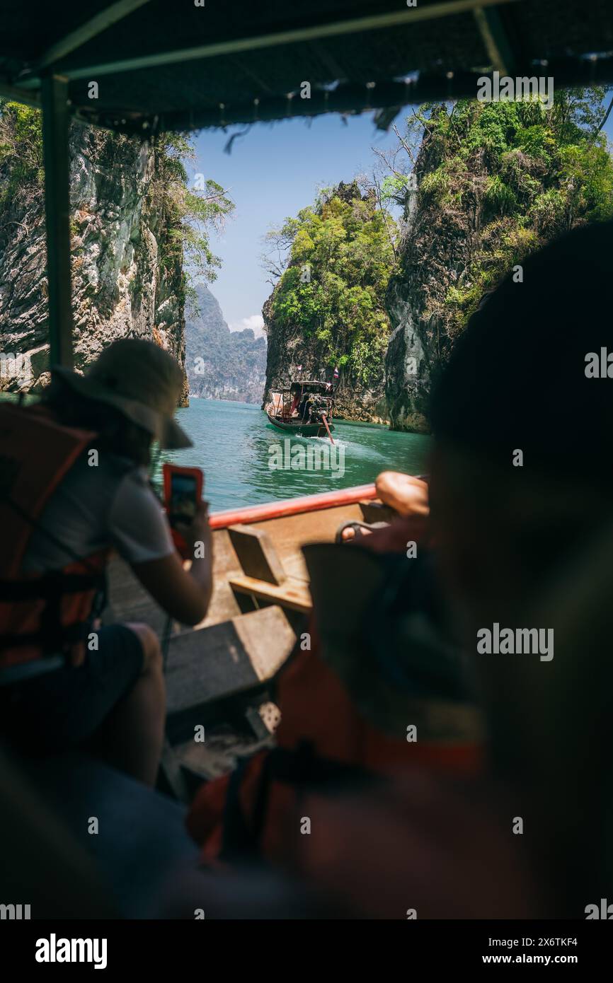 I viaggiatori su una barca sperimentano una gita in barca soleggiata tra le formazioni rocciose. Parco nazionale di Khao Sok, Thailandia Foto Stock