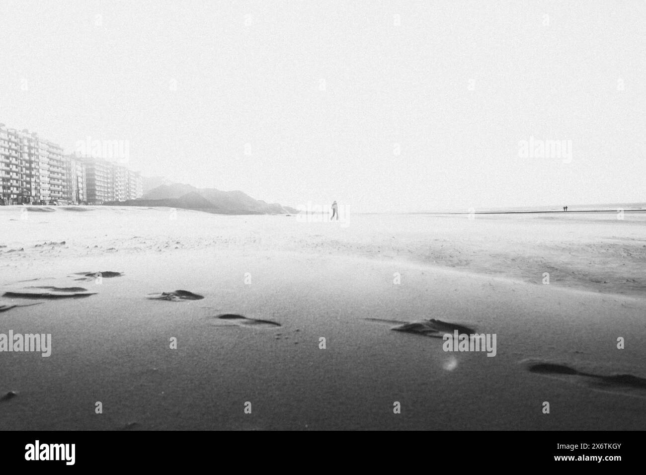 Figura solitaria su una spiaggia vuota in bianco e nero con il mare sullo sfondo. Middelkerke, Belgio Foto Stock