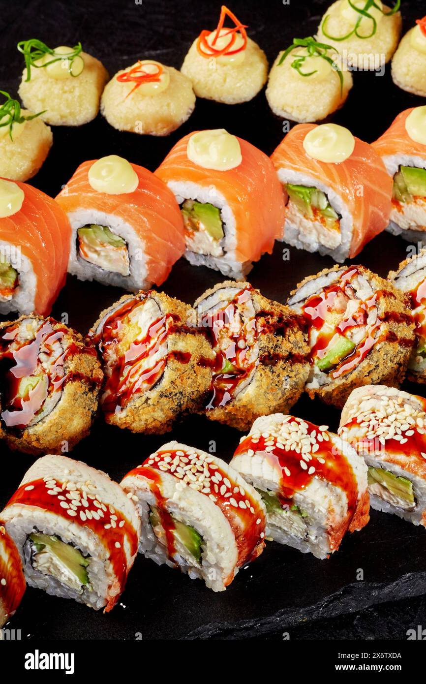 Speciali sushi roll disposti su tavola nera Foto Stock