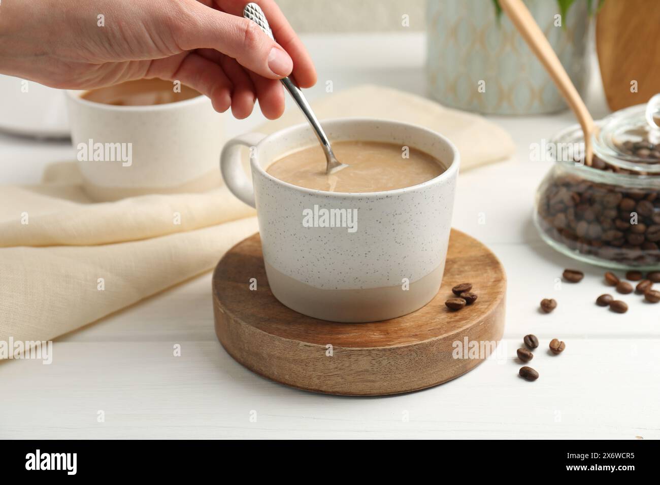 Donna che mescola il caffè con un cucchiaio al tavolo di legno bianco, primo piano Foto Stock