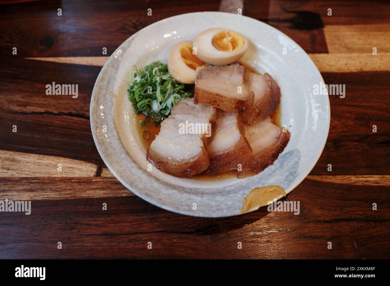 Un piatto splendidamente placcato con succulente fette di maiale chashu, accompagnato da un uovo perfettamente morbido e cipolle verdi fresche. Foto Stock