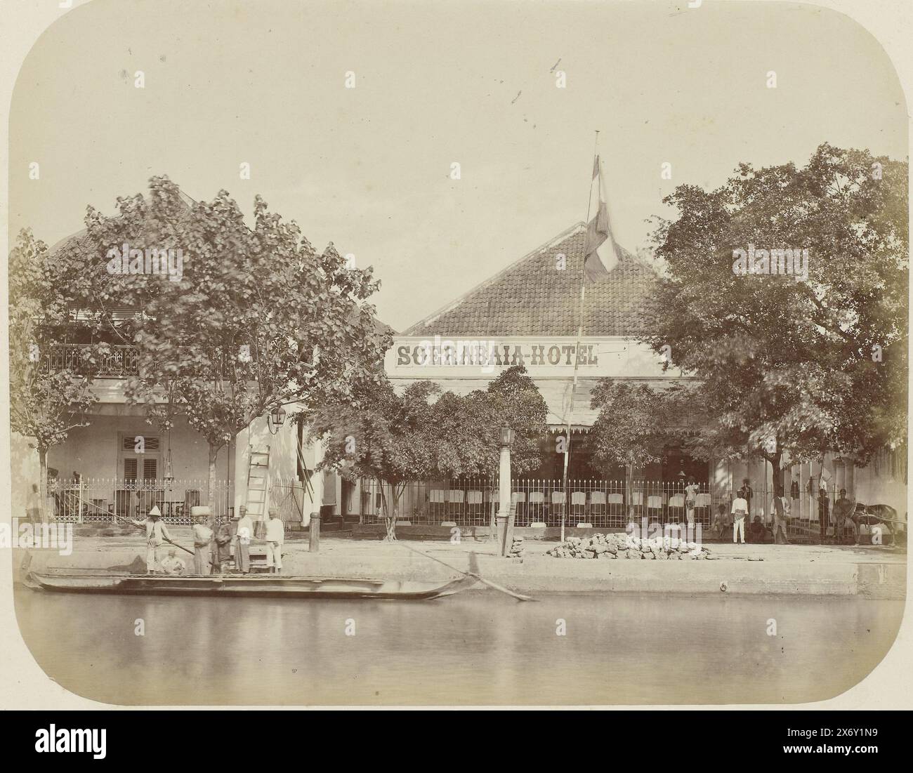 L'hotel Surabaya, l'hotel Surabaya con un proa con sei persone sulla sinistra. La bandiera è stata alzata di fronte all'hotel. Un certo numero di alberi sulla banchina. Parte dell'album fotografico presentato dalla Soerabayasche Association of Sugar Manufacturers a Frederik Beyerinck, residente a Soerabaya., Fotografia, Herman Salzwedel, Soerabayasche Vereeniging van Suikerfabrikanten, Surabaya, 1876 - 1884, supporto fotografico, stampa albume, altezza, 21,8 cm x larghezza, 27,9 cm Foto Stock