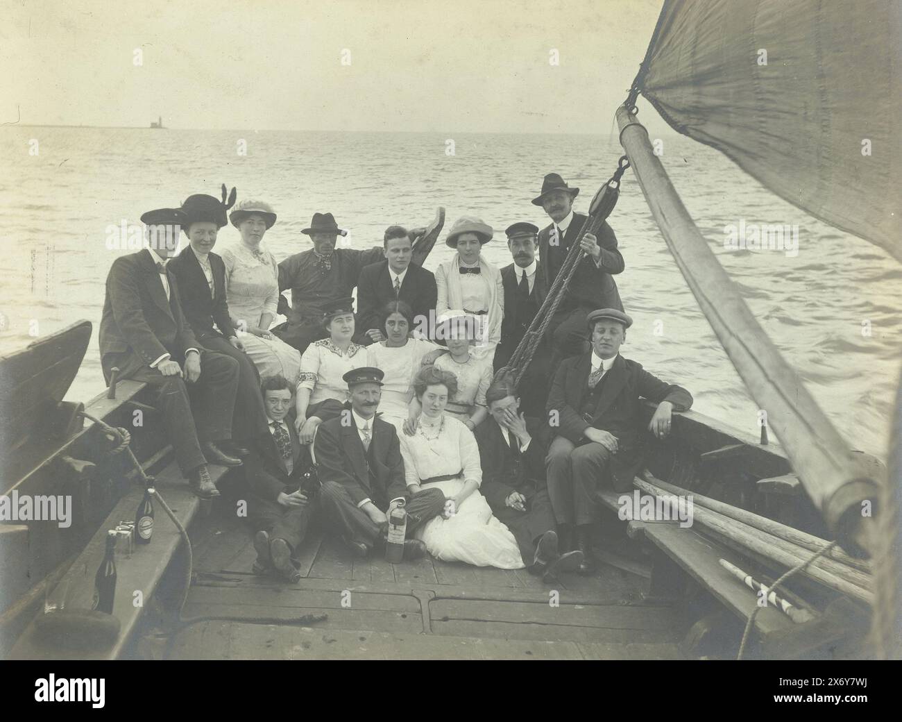 Ritratto di gruppo di un gruppo su una nave a vela, sette donne e nove uomini seduti sulla poppa di una nave a vela. Bottiglie di birra a sinistra sul divano., fotografia, anonima, Paesi Bassi, c. 1915 - c. 1920, supporto fotografico, stampa in argento gelatina, altezza, 116 mm x larghezza, 157 mm Foto Stock