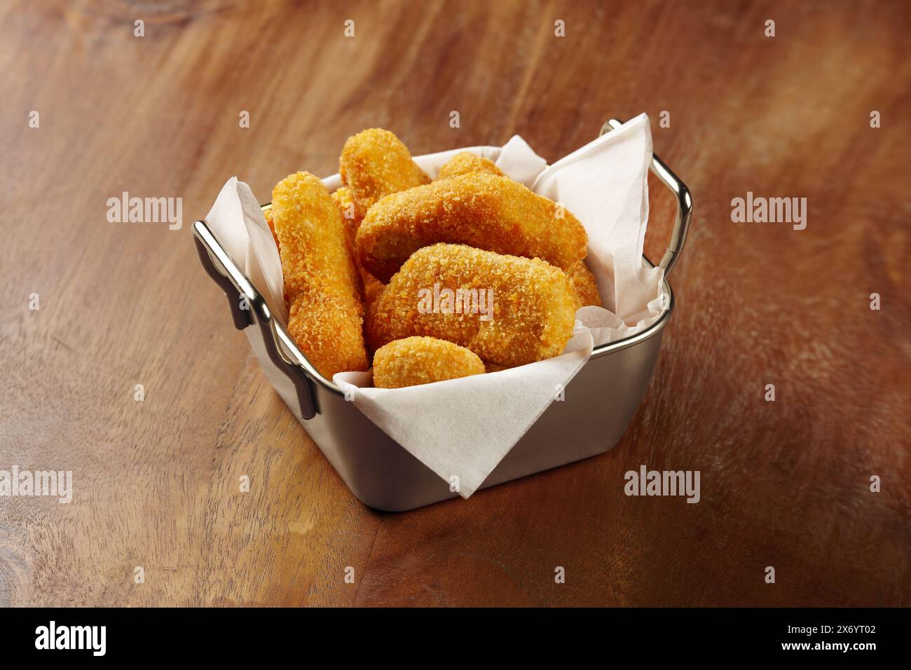 Una porzione di pepite di pollo in un unico contenitore di latta al centro di un tavolo di legno Foto Stock