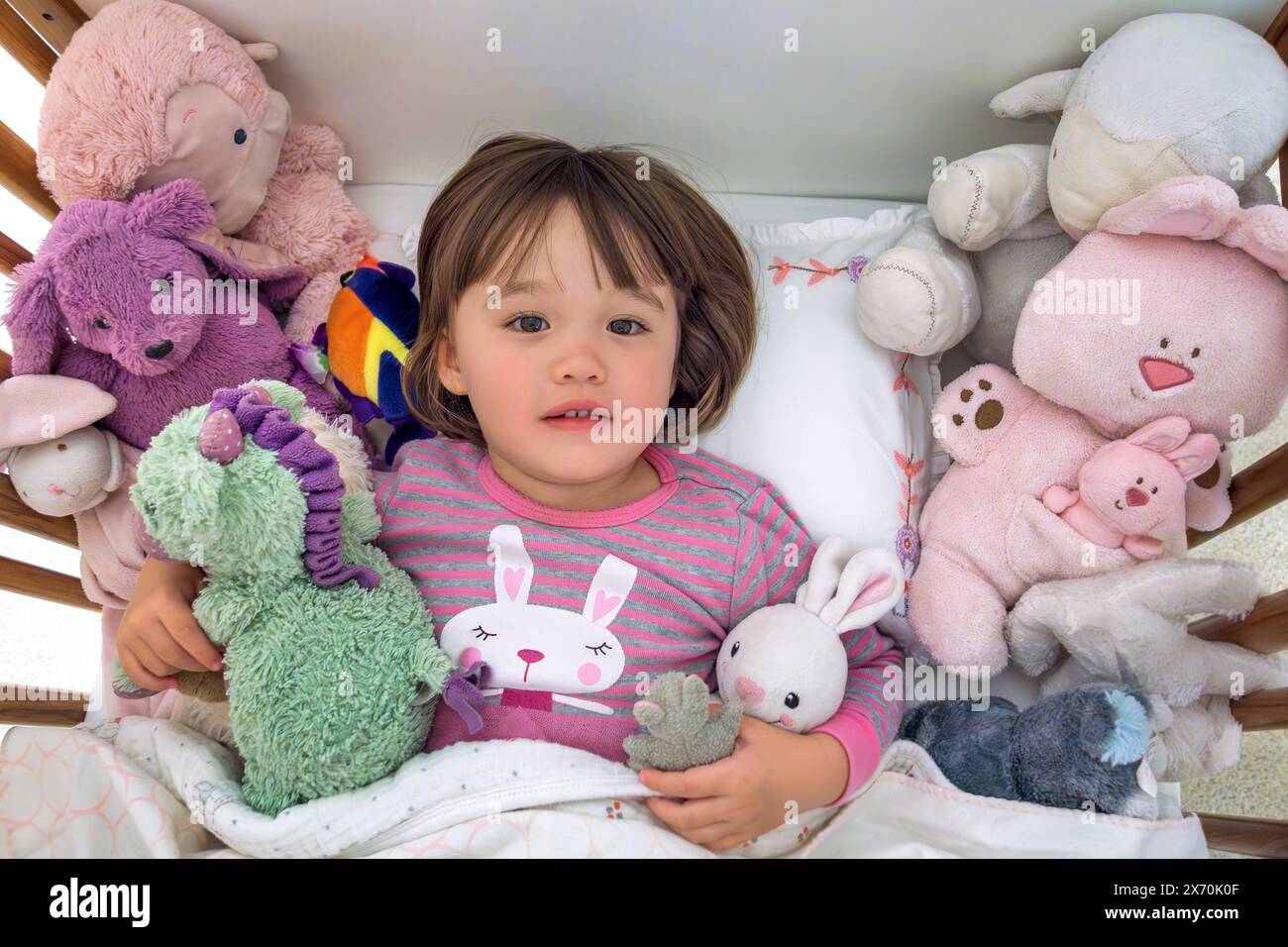 Bimbo che si sdraia all'interno della culla con i suoi giocattoli imbottiti Foto Stock