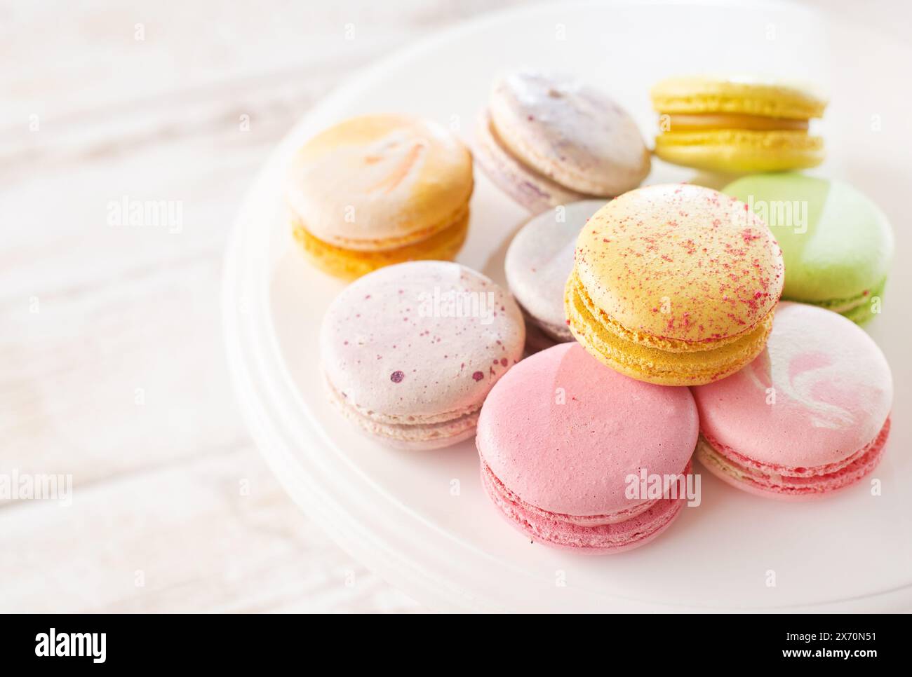 Macaron multicolore su sfondo in legno con luci e ombre soffuse. Delicati macaron sul tavolo su sfondo chiaro. Foto Stock