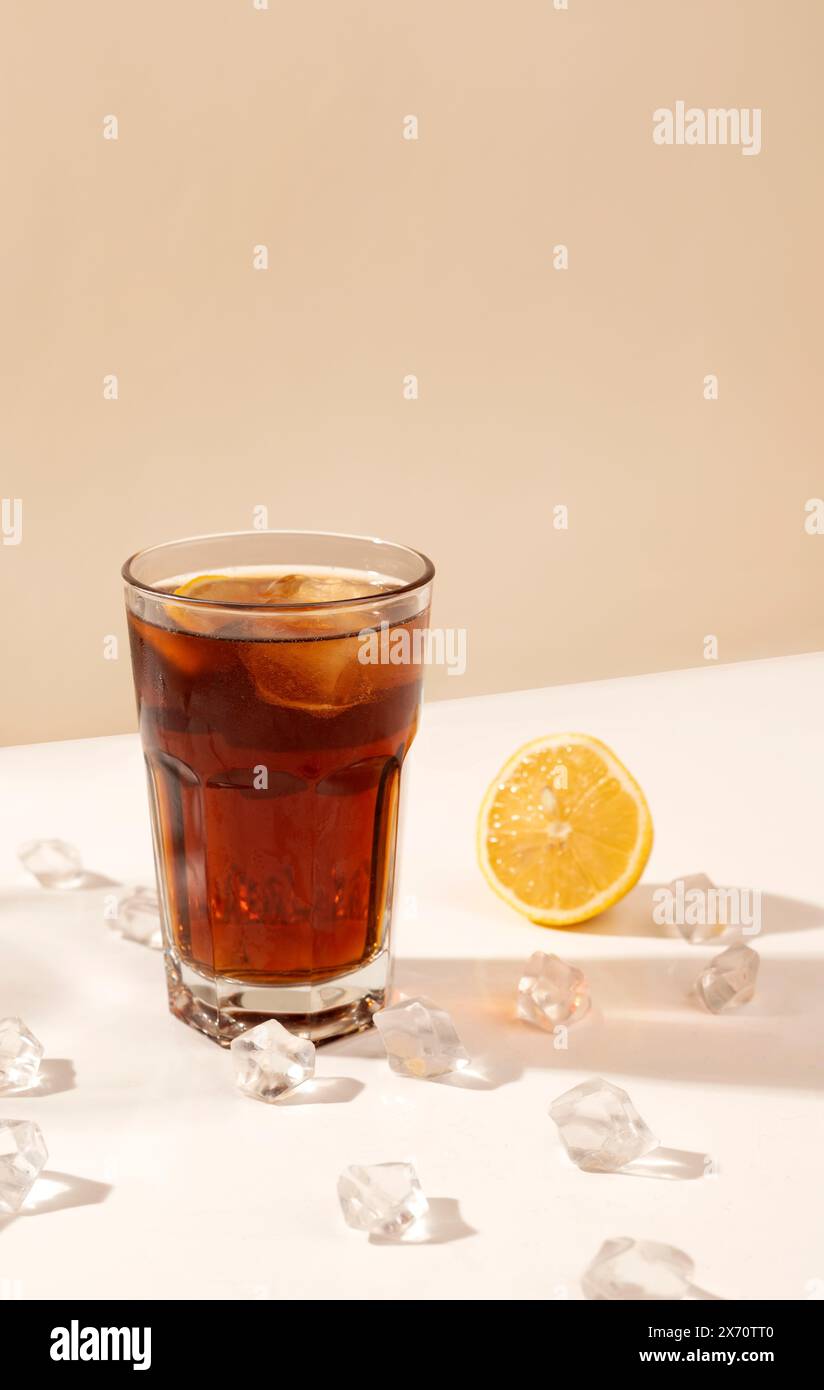 bicchiere di bevanda alcolica sul tavolo con cubetti di ghiaccio e limone. ombra lunga. concetto di festa e cocktail. rum e cola. Foto Stock