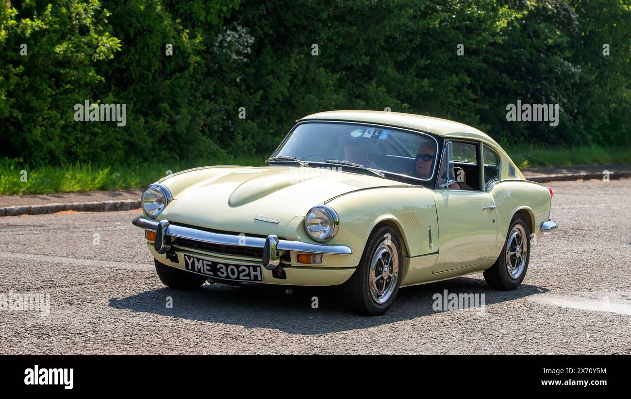 Stoke Goldington, Regno Unito - 11 maggio 2024: 1970 auto Triumph GT6 gialla che guida su una strada britannica Foto Stock