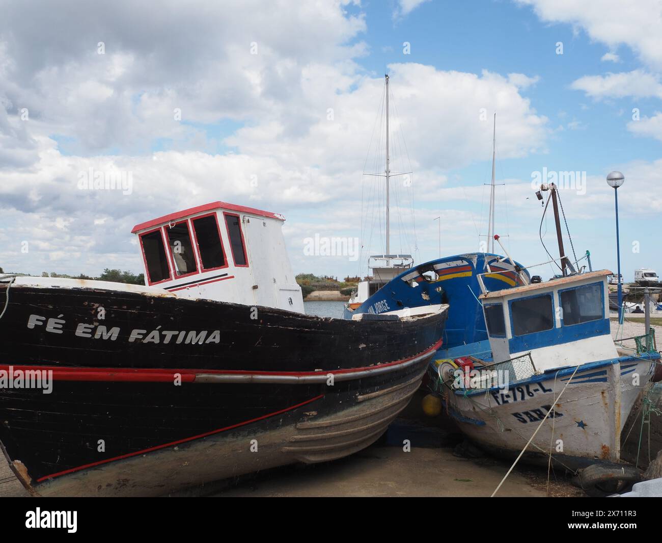 Barca in legno di colore bianco e rosso Fé em Fátima e altra barca sullo scalo al porto di Fuseta, Portogallo. Il nome è un titolo cattolico di Maria madre di Gesù Foto Stock