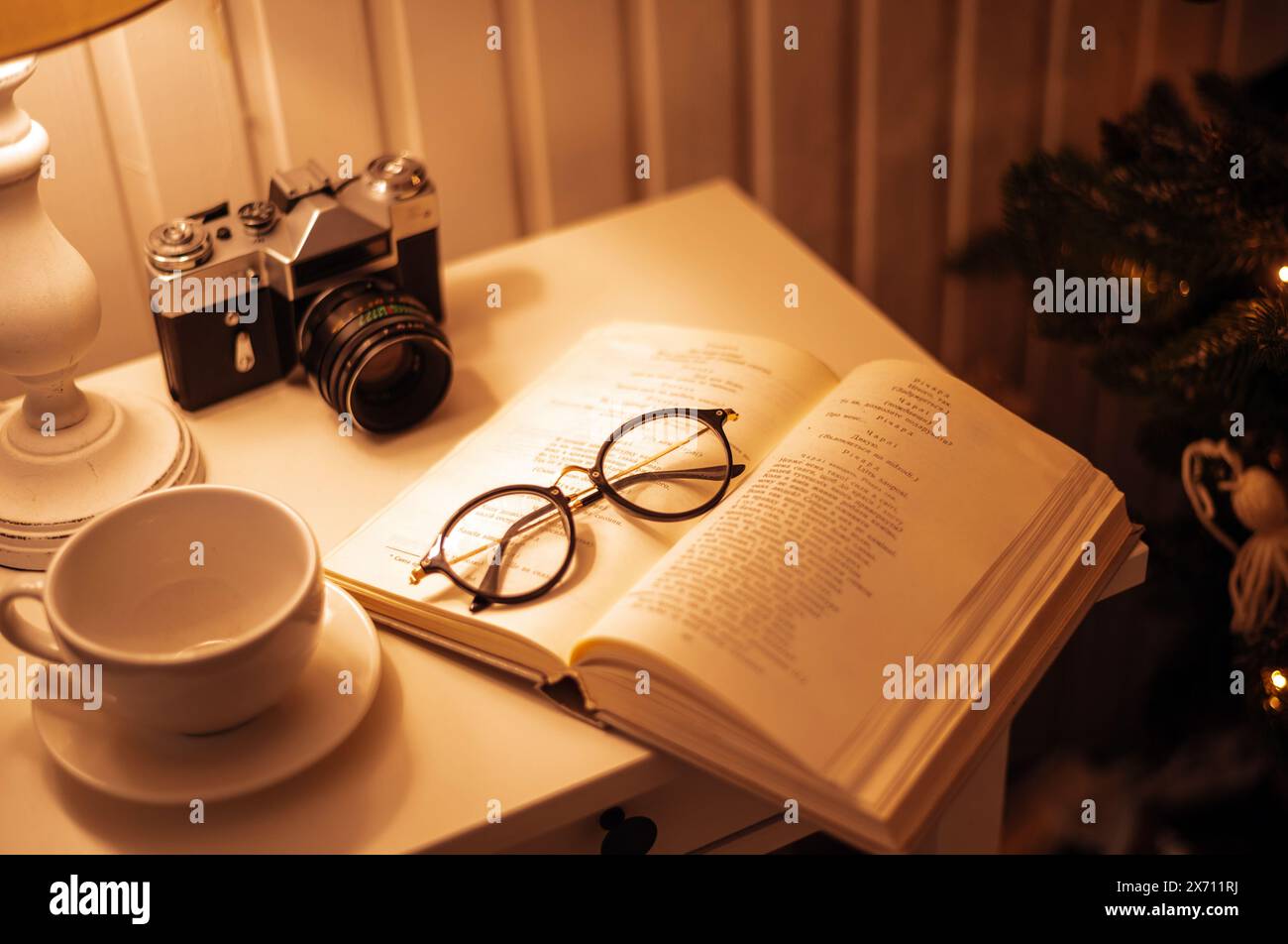 28 novembre 2020. Kiev, Ucraina. Atmosfera casalinga d'epoca. Fotocamera retrò, bicchieri, tazza da caffè e libro sul tavolo con lampada. Messa a fuoco selettiva. Foto Stock
