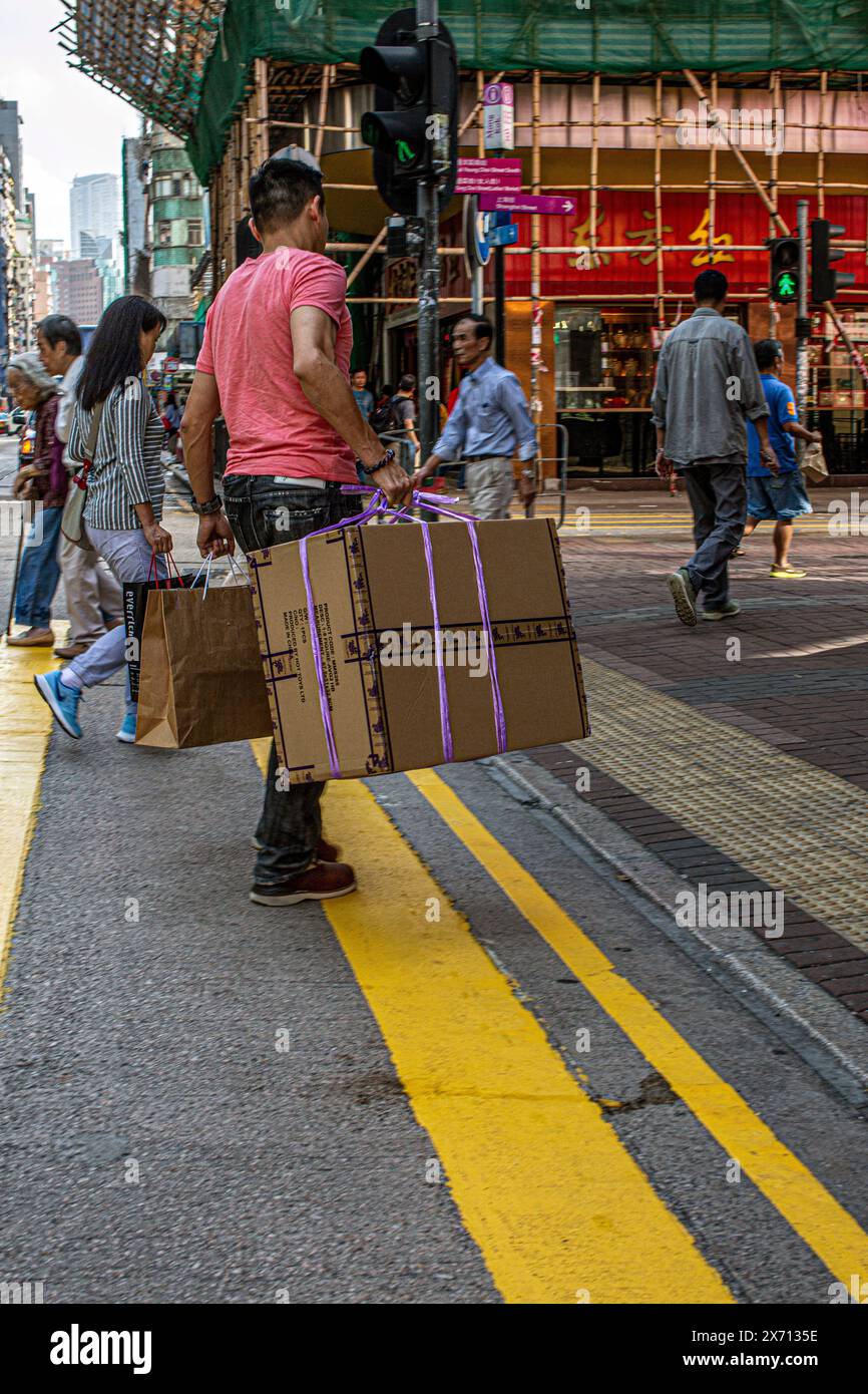 Uomo che trasporta scatole pesanti con altre persone sulla strada pedonale di Hong Kong, Cina, Asia. Foto Stock