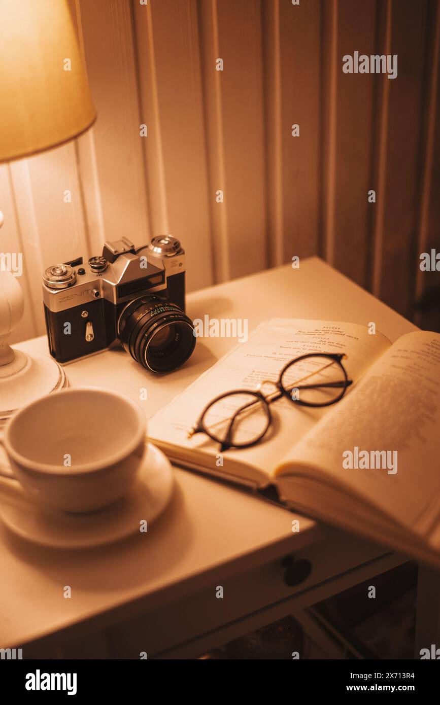 28 novembre 2020. Kiev, Ucraina. Atmosfera casalinga d'epoca. Fotocamera retrò, bicchieri, tazza da caffè e libro sul tavolo con lampada. Messa a fuoco selettiva. Foto Stock
