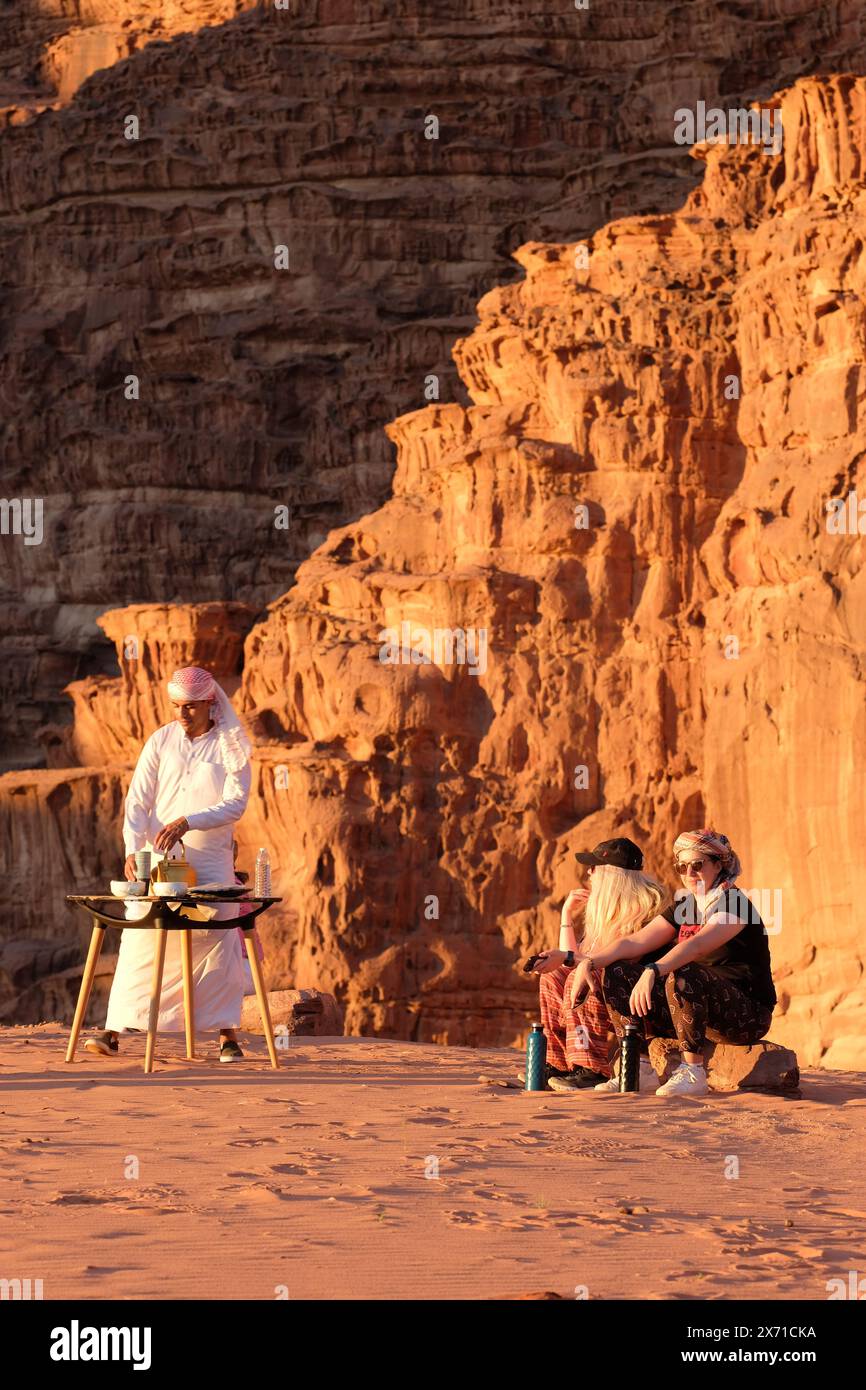 Wadi Rum, i turisti giordani si godono un tramonto serale in un accampamento turistico nel deserto a Wadi Rum con un beduino che serve tè - agosto 2023 Foto Stock