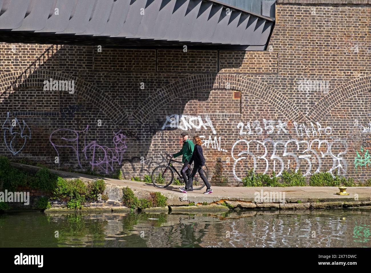 Vista dal Parco naturale di Camley Street del Regents Canal People con passeggiata in bicicletta sotto il ponte con graffiti murali 2024 Londra Inghilterra Regno Unito KATHY DEWITT Foto Stock