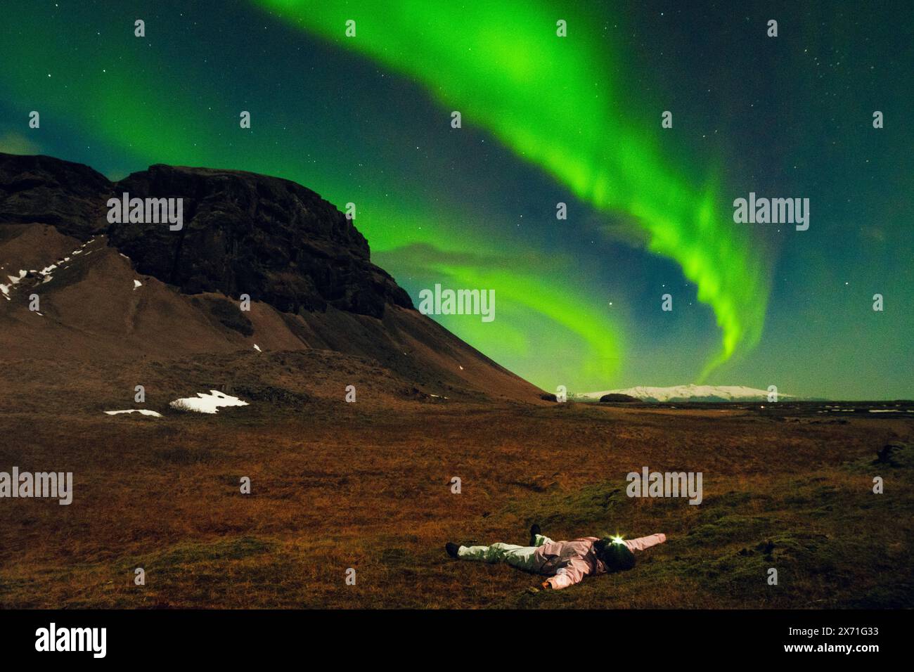 Donna che guarda l'aurora boreale giacere su prati erbosi da sola in Islanda. Donna romantica nel paesaggio primaverile della notte islandese Islanda viaggio inseguendo Foto Stock
