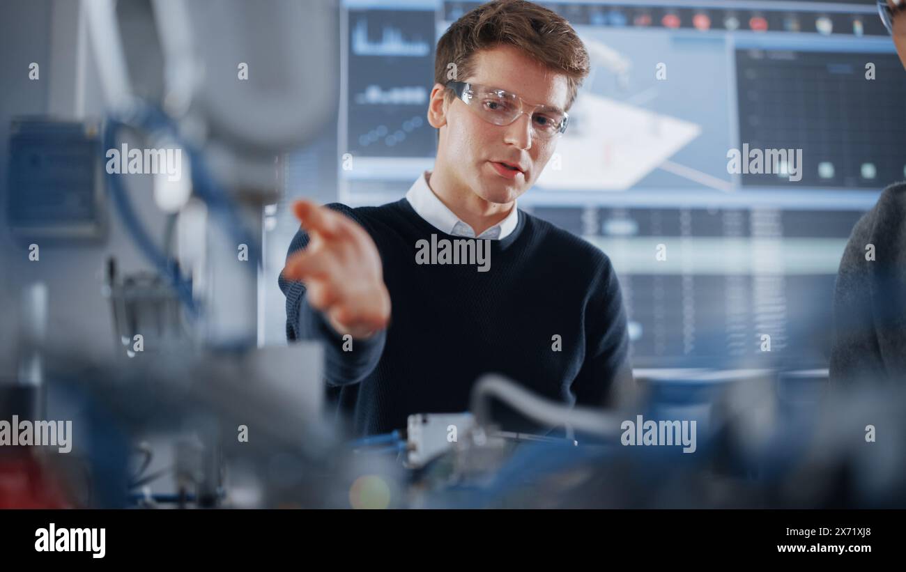 Studenti curiosi che condividono idee tra loro mentre lavorano insieme alla modifica delle funzioni del braccio meccanico per il progetto di ingegneria presso la scuola in officina. Concetto di educazione informatica Foto Stock