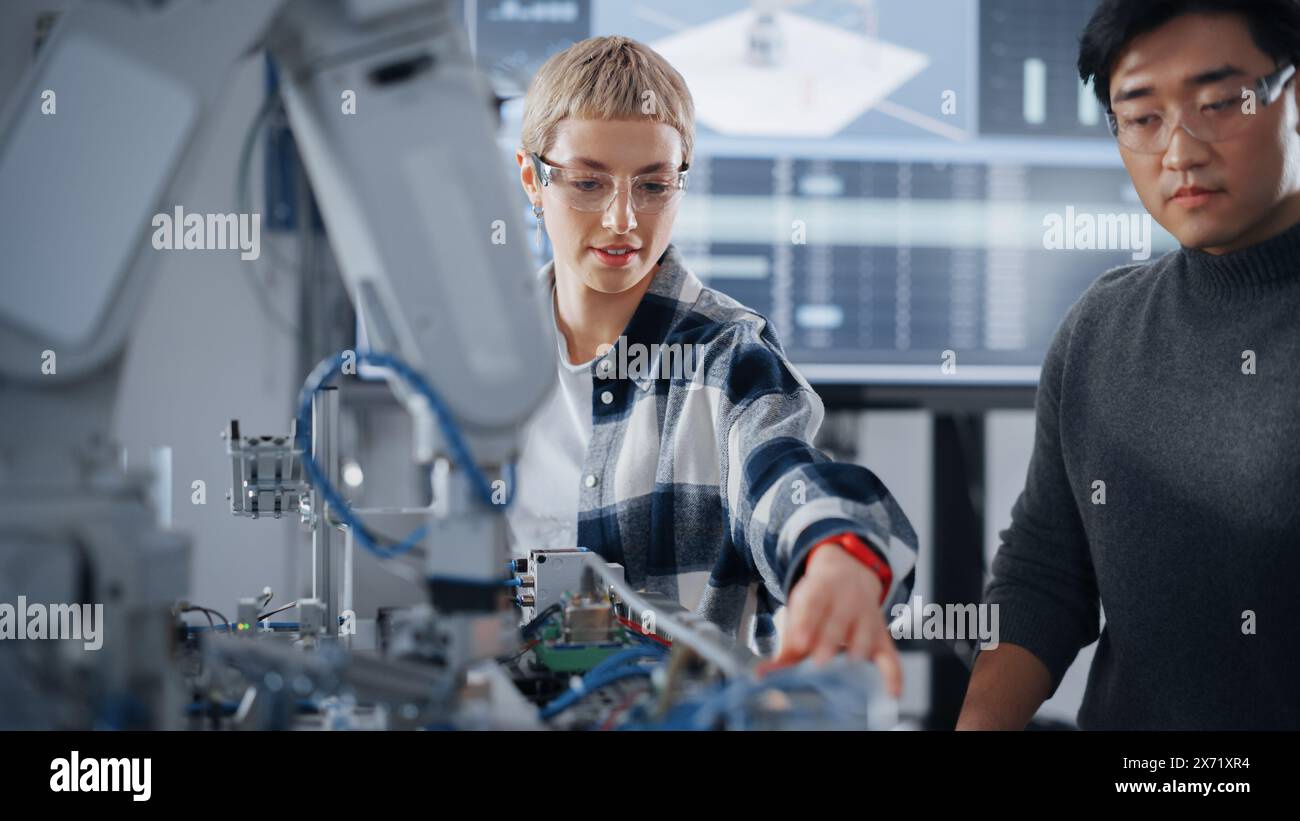 Studenti curiosi che condividono idee tra loro mentre lavorano insieme alla modifica delle funzioni del braccio meccanico per il progetto di ingegneria presso la scuola in officina. Concetto di educazione informatica Foto Stock
