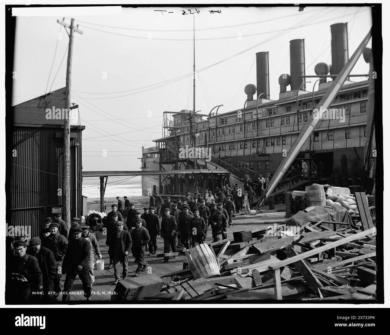 Mezzogiorno, Str. Seeandbee, '455-T' in negativo., foto mostra un equipaggio di un cantiere che lascia il piroscafo Seeandbee per il quale probabilmente stavano finendo il lavoro. E' al cortile di Orleans Street a Detroit. Fu lanciata a Wyandotte come scafo vuoto e immediatamente rimorchiata a Orleans Street per ottenere i suoi motori, caldaie e sovrastruttura. Sulla destra è possibile vedere le cesoie utilizzate per sollevare caldaie e macchinari pesanti in nuovi recipienti. La Seeandbee salpò nel giugno del 1913. (Fonte: W. Worden and C. Seavey, 2020), 'Ship Bldg. Co.' su negative., Detroit Publishing Co. No X 1291., omaggio; storico statale Foto Stock
