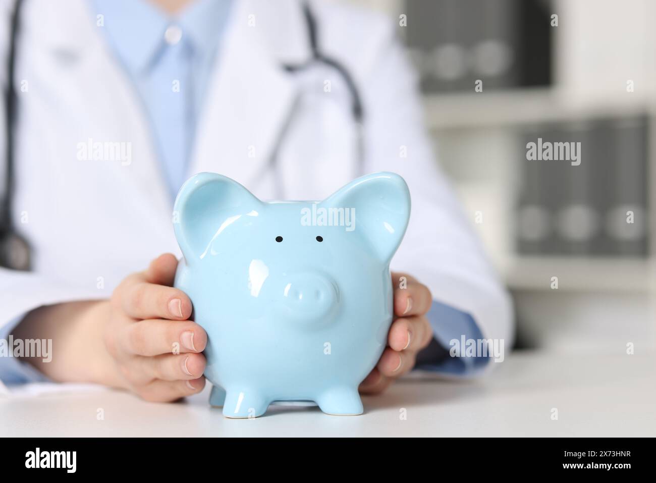 Dottore con salvadanaio al tavolo bianco all'interno, primo piano. Spazio per il testo Foto Stock