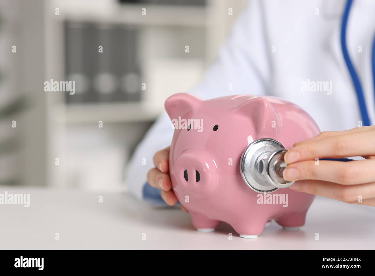 Dottore con salvadanaio al tavolo bianco all'interno, primo piano. Spazio per il testo Foto Stock