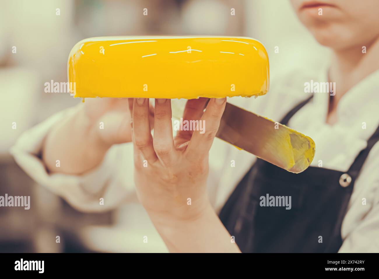 Il dolcificante leviga la glassa gialla su una torta con una spatola. Preparazione della torta da parte di un pasticcere professionista. Foto Stock