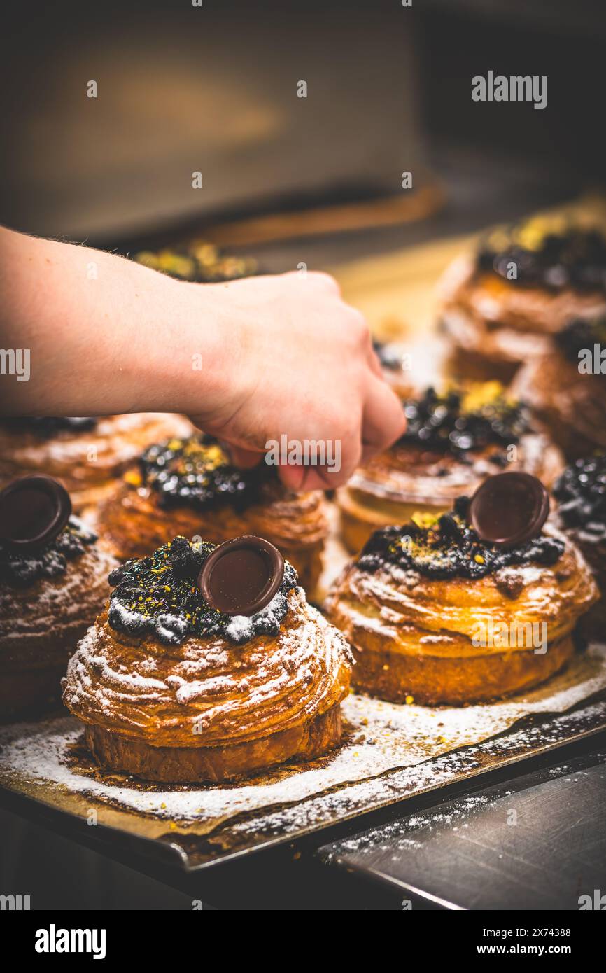 La mano del pasticciere decora le tartarughe con cioccolato. Preparazione delle tartine da parte di un pasticcere professionista. Foto Stock