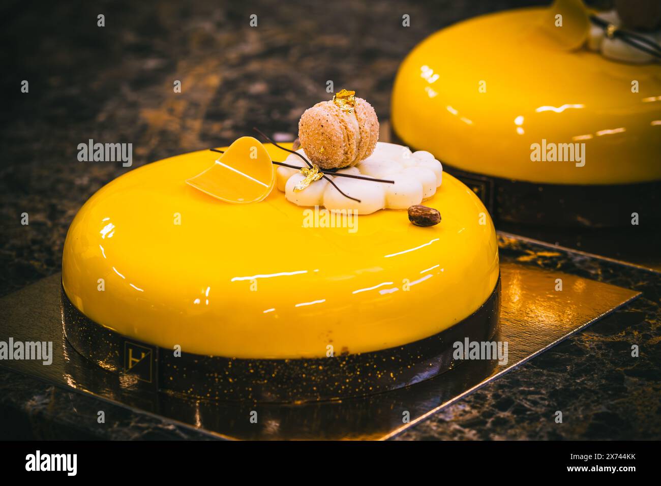 Crostata con uno smalto giallo, macaron, biscotti, cioccolato e decorazioni in oro, sfondo scuro Foto Stock