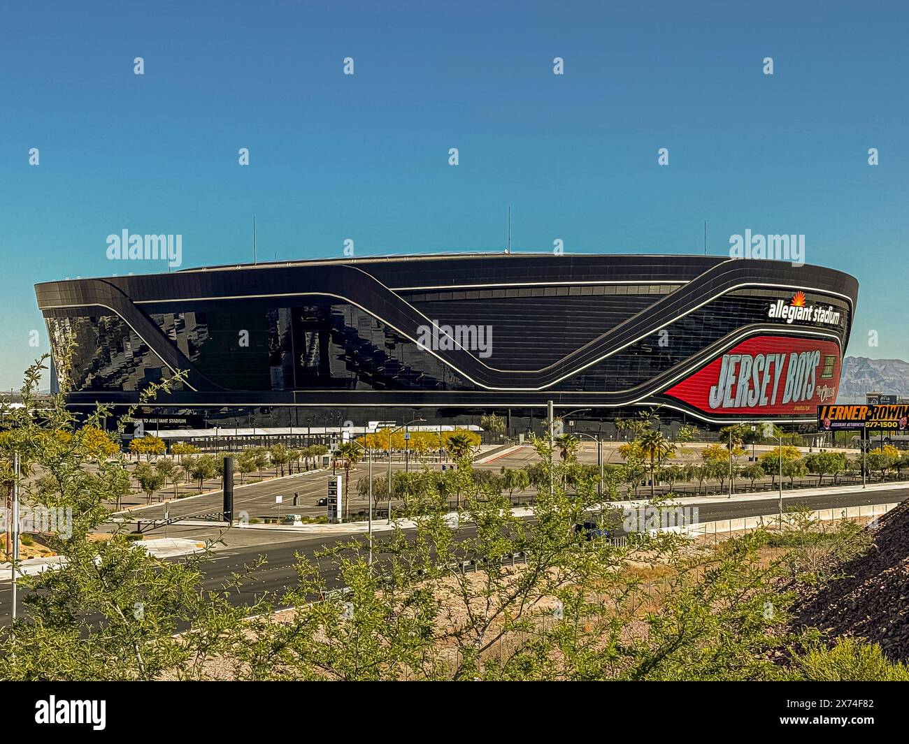 Las Vegas, Nevada, USA - 12 maggio 2024: Primo piano del Black Allegiant Stadium con il cartello dei Jersey Boys sotto il cielo blu. Parcheggio vuoto e vegetazione verde Foto Stock