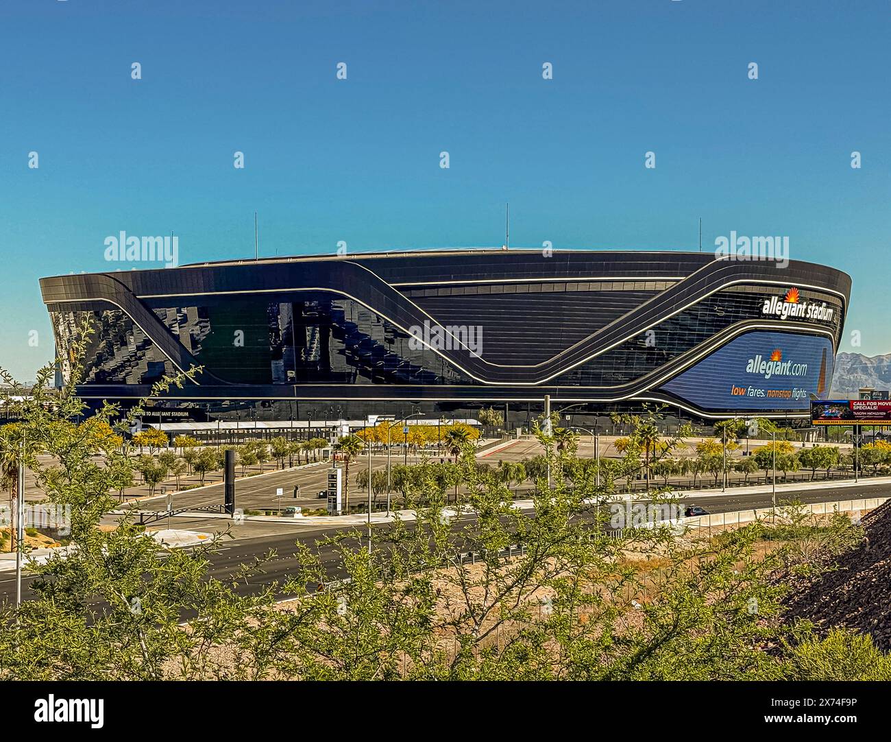 Las Vegas, Nevada, Stati Uniti - 12 maggio 2024: Primo piano dello stadio Black Allegiant con cartello della compagnia aerea sotto il cielo blu. Parcheggio vuoto e vegetazione verde Foto Stock