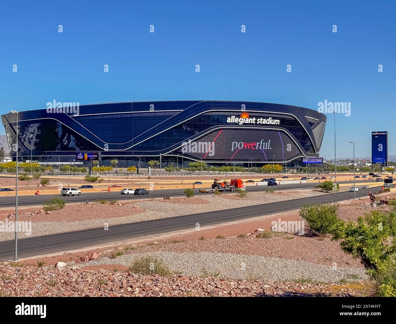 Las Vegas, Nevada, Stati Uniti - 12 maggio 2024: Black Allegiant Stadium dietro l'interstate 15 con un potente cartello sotto il cielo blu. Parcheggio vuoto, auto su strada, e gr Foto Stock