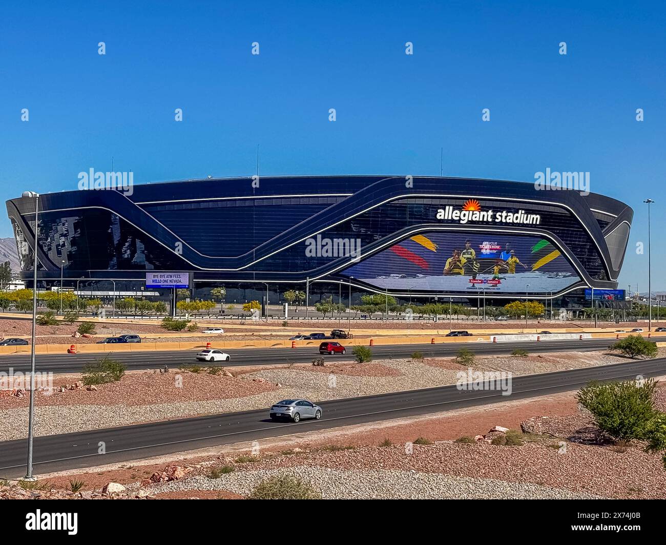 Las Vegas, Nevada, Stati Uniti - 12 maggio 2024: Black Allegiant Stadium dietro l'interstate 15 con cartello internazionale di calcio sotto il cielo blu. Parcheggio vuoto, auto accese Foto Stock