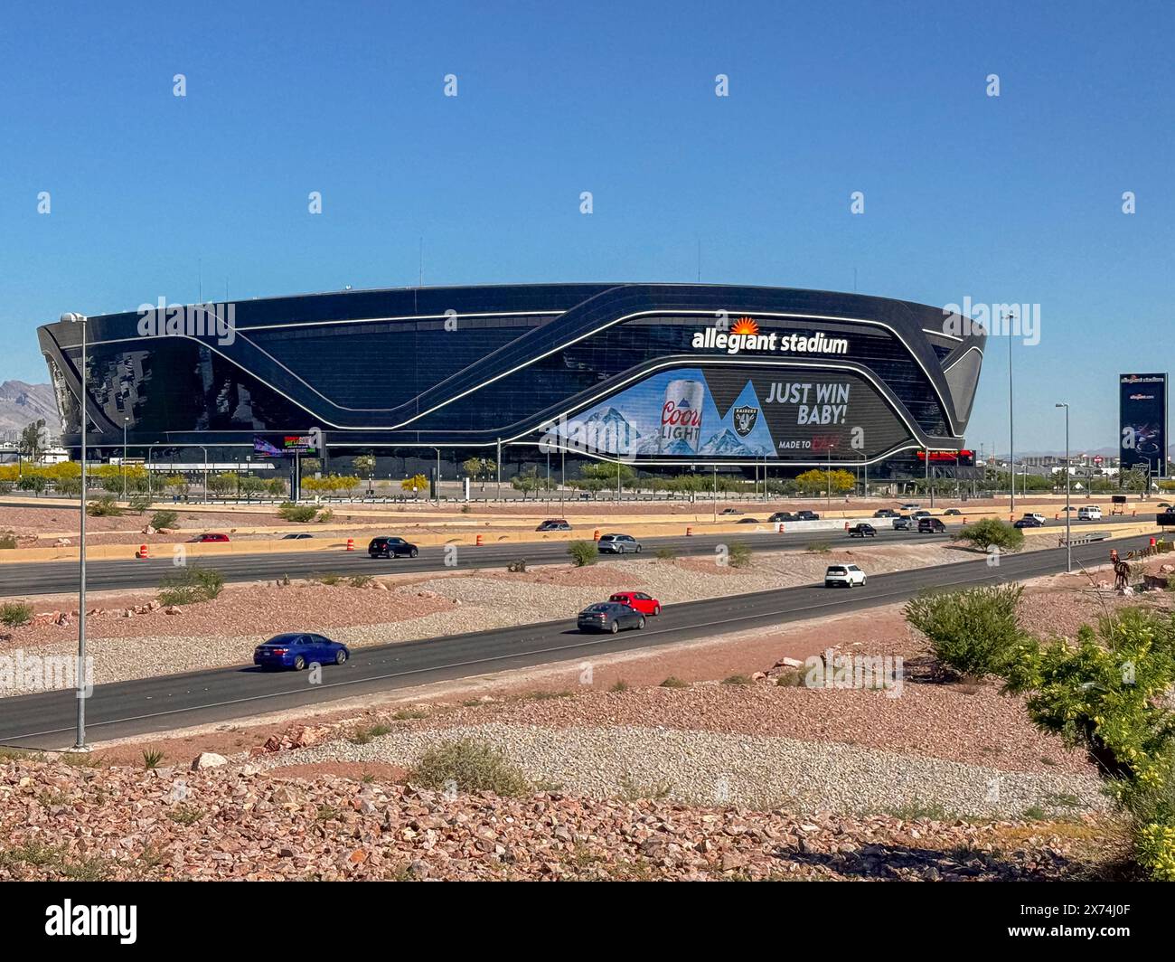 Las Vegas, Nevada, Stati Uniti - 12 maggio 2024: Black Allegiant Stadium dietro l'interstate 15 con cartello Coors Light sotto il cielo blu. Parcheggio vuoto, auto su strada, e. Foto Stock