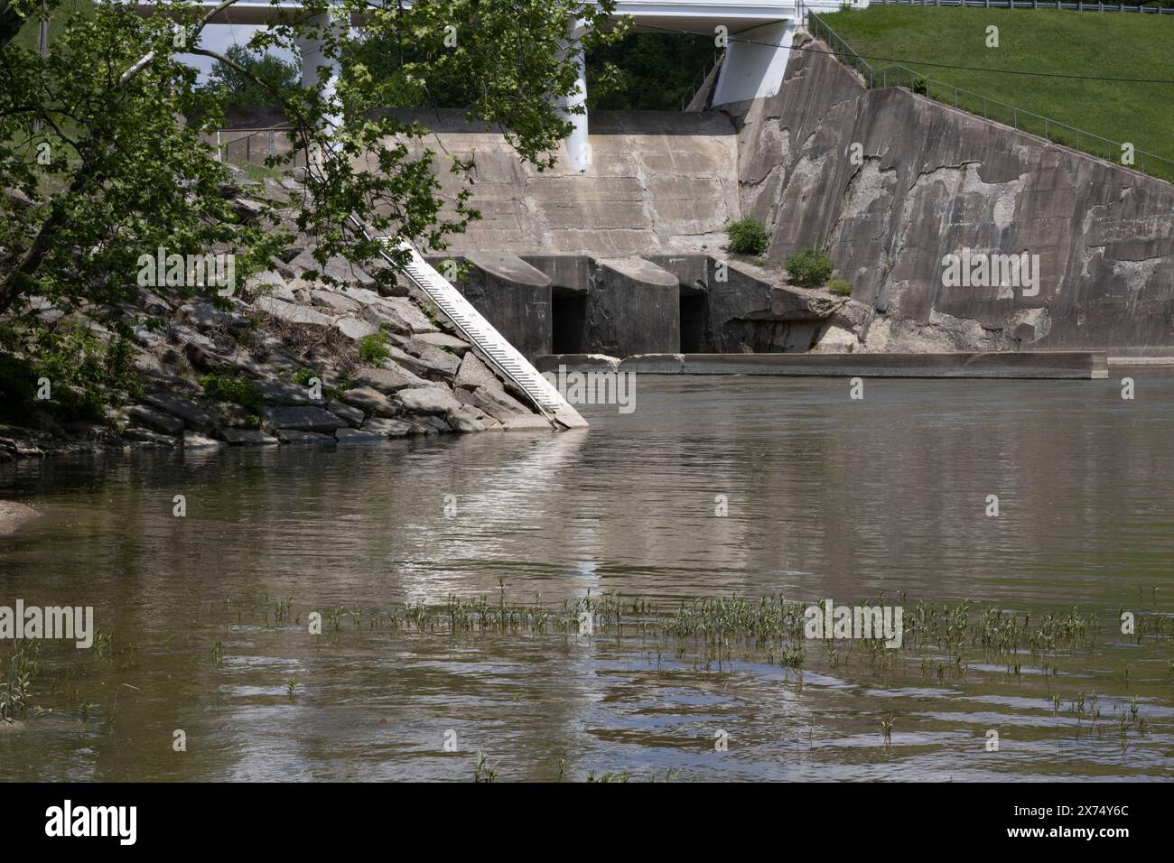 Spillway & Ladder: Cielo limpido, corpo d'acqua, spillway di cemento, scala, circondato da vegetazione lussureggiante. Sereno e strutturato. Foto Stock