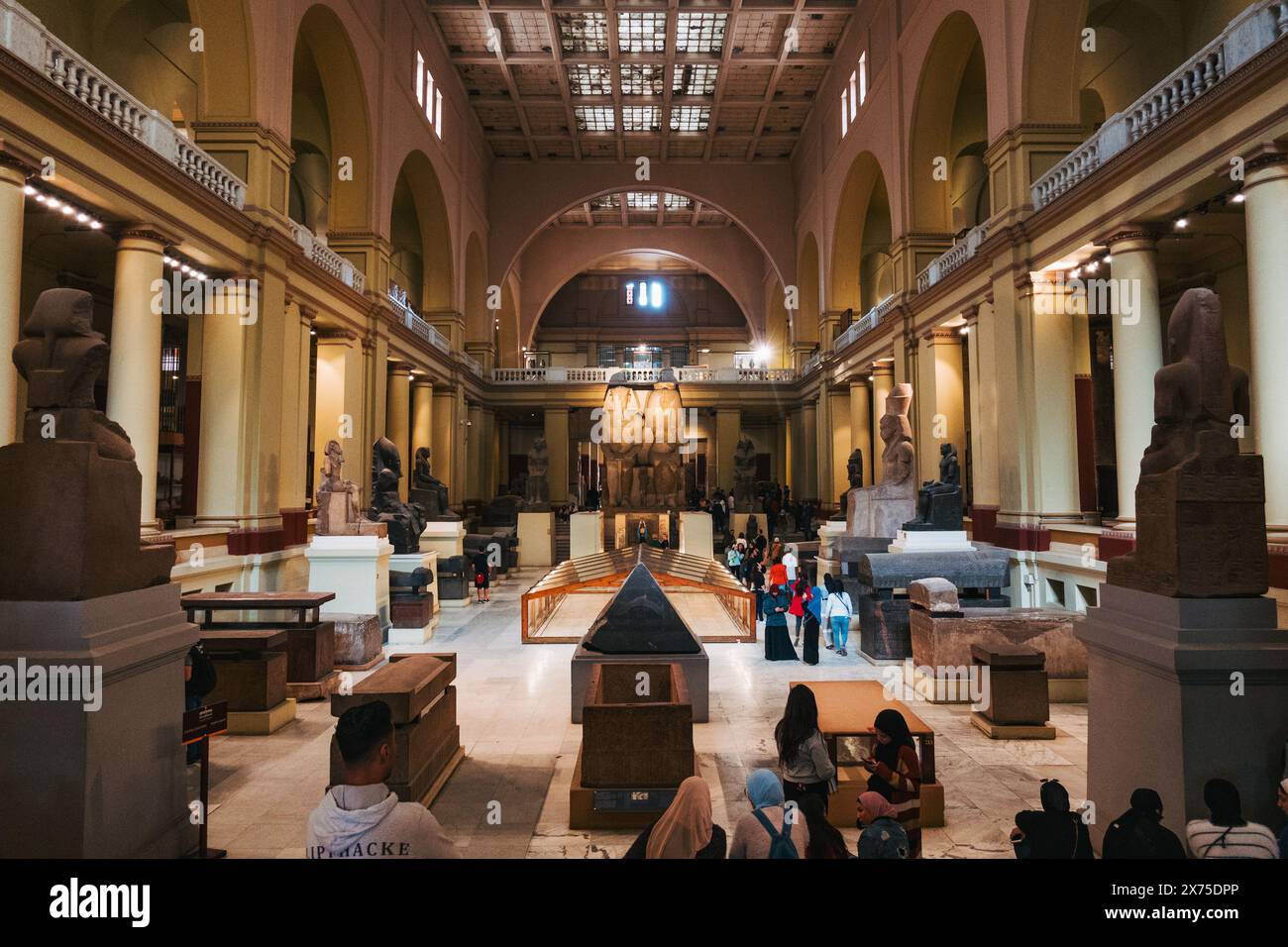 Sala principale del Museo Egizio del Cairo, piena di sarcofagi, statue e turisti, sotto un alto soffitto ad arco e un'architettura simmetrica Foto Stock