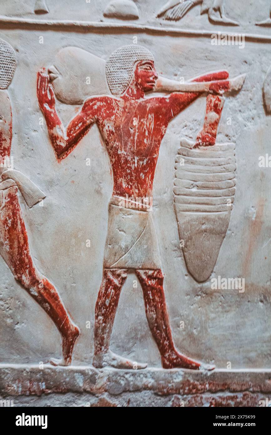 Tombe dipinte in rilievo di Saqqara che mostrano un operaio del Vecchio Regno che sprema l'uva o impastare, con pigmento rosso vibrante e intaglio dettagliato. Foto Stock