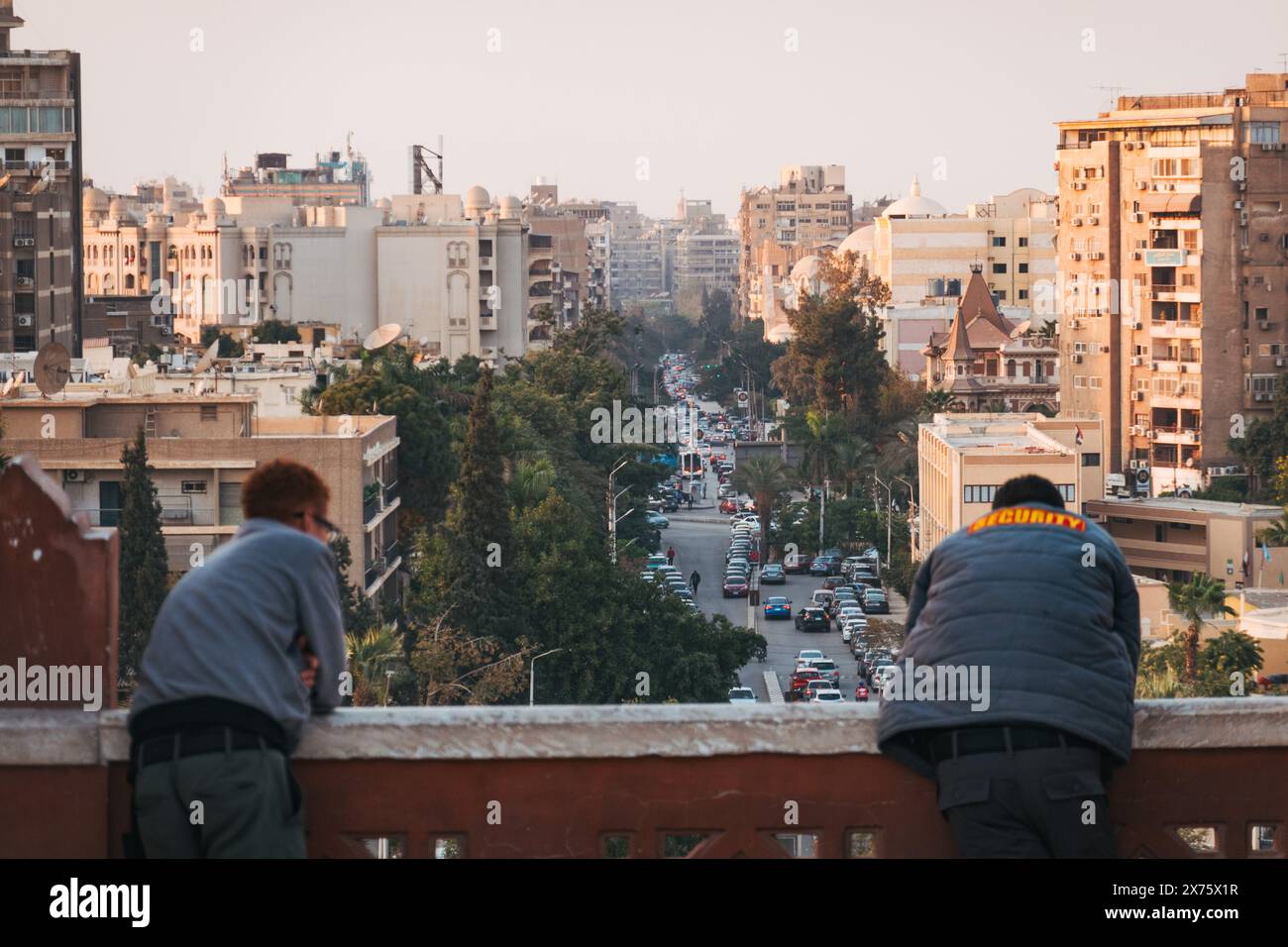 Le guardie di sicurezza si appoggiano sulla balaustra rossa in arenaria del Palazzo del Barone Empain, affacciata sulle trafficate strade urbane di Eliopoli, il Cairo, al tramonto Foto Stock