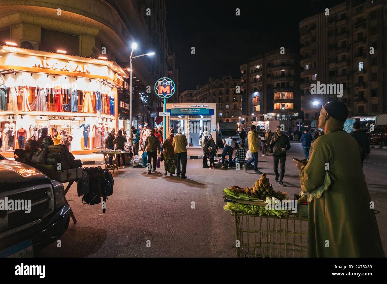 Scena di strada notturna vicino alla stazione della metropolitana Nasser al Cairo, Egitto, con venditori ambulanti, acquirenti, espositori di abbigliamento luminosi, e vivace attività urbana Foto Stock