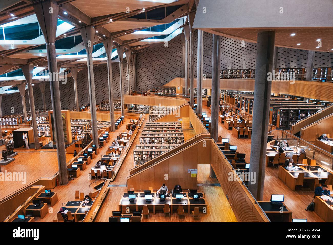 Colonne in cemento e scaffali e scrivanie in legno all'interno della Bibliotheca Alexandrina, una vasta biblioteca ad Alessandria, in Egitto Foto Stock