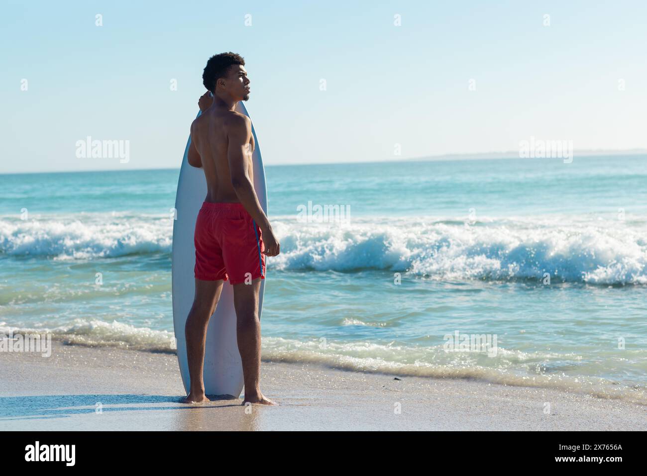 In spiaggia, giovane birazziale in piedi da solo, guardando il mare Foto Stock