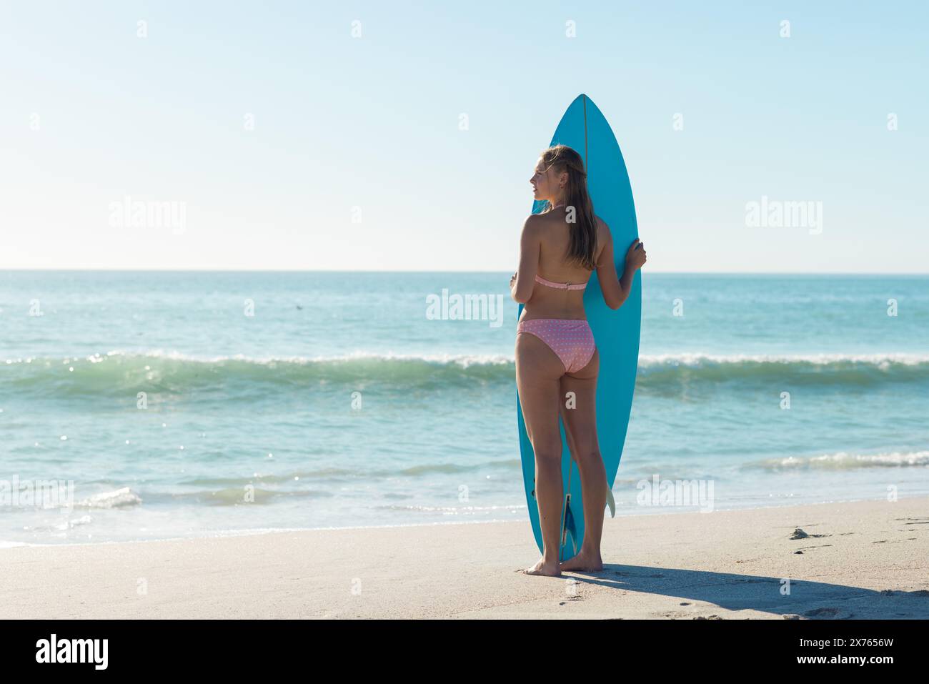 In spiaggia, giovane donna caucasica con tavola da surf e bikini rosa Foto Stock