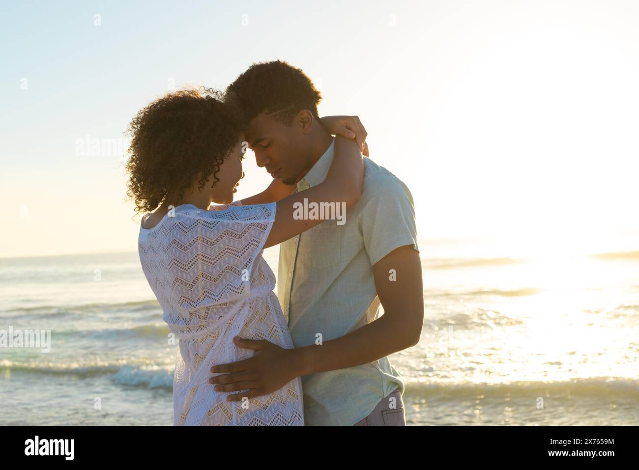 In spiaggia, coppie diverse che abbracciano, il tramonto illumina il cielo Foto Stock