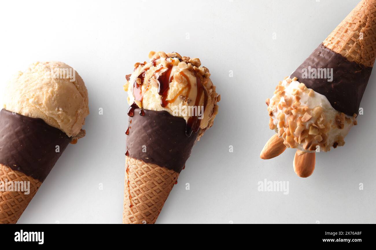 Dettaglio di tre coni di gelato di vari gusti con coni di cioccolato su sfondo bianco. Foto Stock