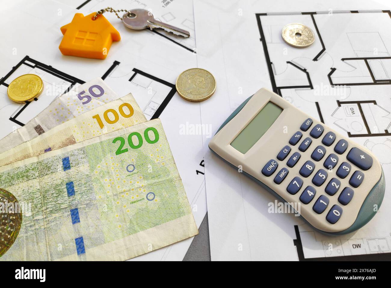 Primo piano su alcune banconote della corona danese (DKK), una chiave domestica e una calcolatrice in cima ai piani di costruzione. Foto Stock