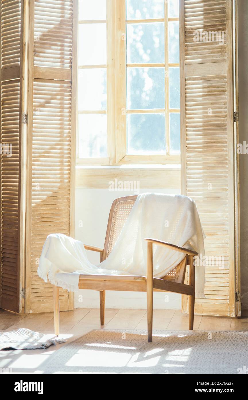 Poltrona in legno con plaid contro finestre con persiane, composizione della stanza e luce solare. Foto di alta qualità Foto Stock