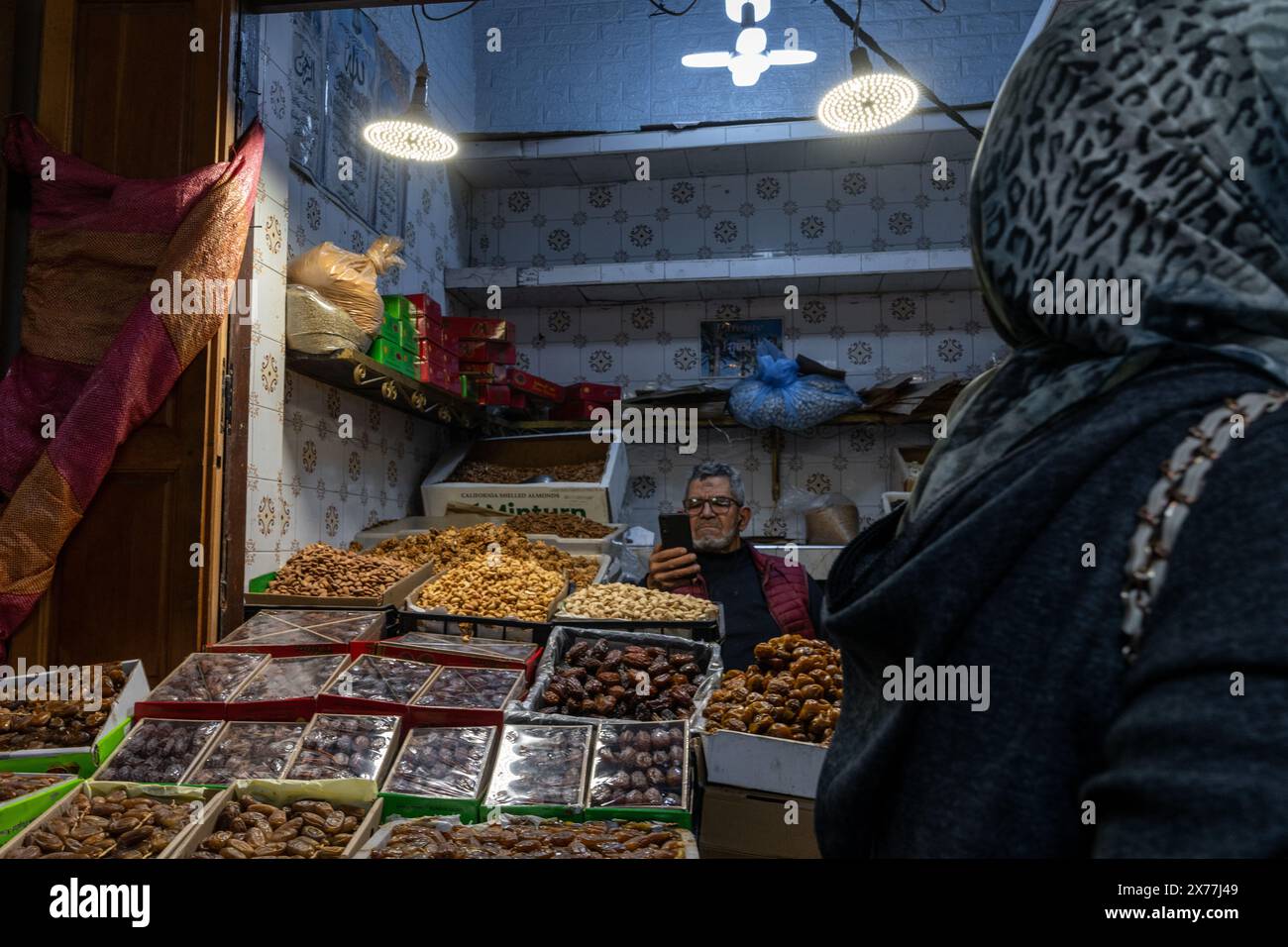 Fez, Marocco - 4 marzo 2024: Negoziante presso il suo stand che vende le date e un cliente di passaggio nel mercato nel centro di Fez Foto Stock