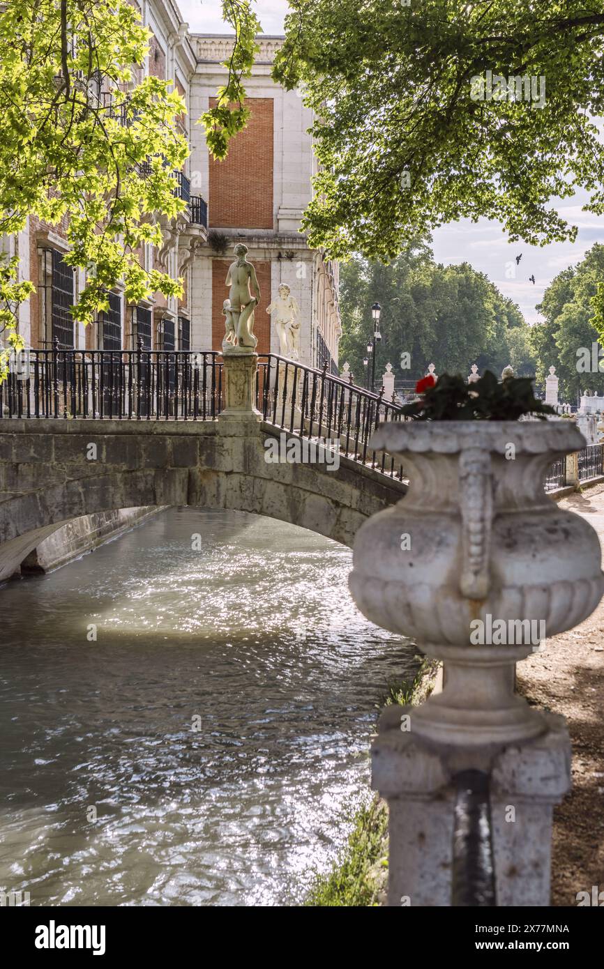 Un canale d'acqua attraverso pareti in pietra che passa attraverso un parco monumentale con splendidi ponti in pietra tra la vegetazione e gli alberi frondosi ad Aranjuez, Spa Foto Stock