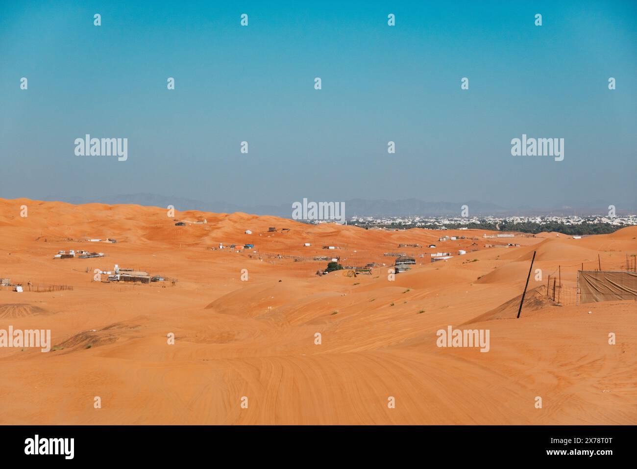 Dune arancioni di Sharqiyah Sands in Oman, con campi desertici sparsi e insediamenti lontani sotto un cielo azzurro Foto Stock