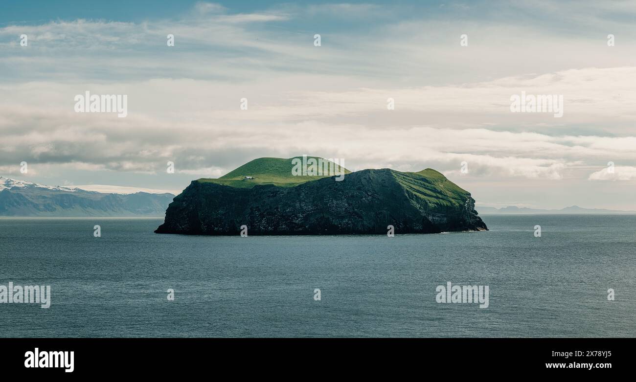 Una vista panoramica di una piccola isola isolata a Vestmannaeyjar (Isole Westman), Islanda, caratterizzata da scogliere verdi e una casa solitaria. Foto Stock