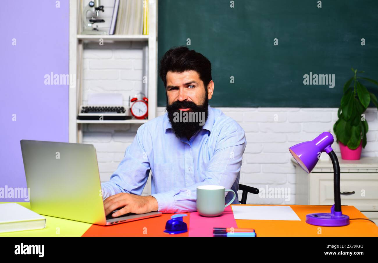 Studente di sesso maschile che studia online all'università. Istruzione e conoscenza. Insegnante barbuta in classe seduto alla scrivania lavorando su un computer portatile. E Foto Stock